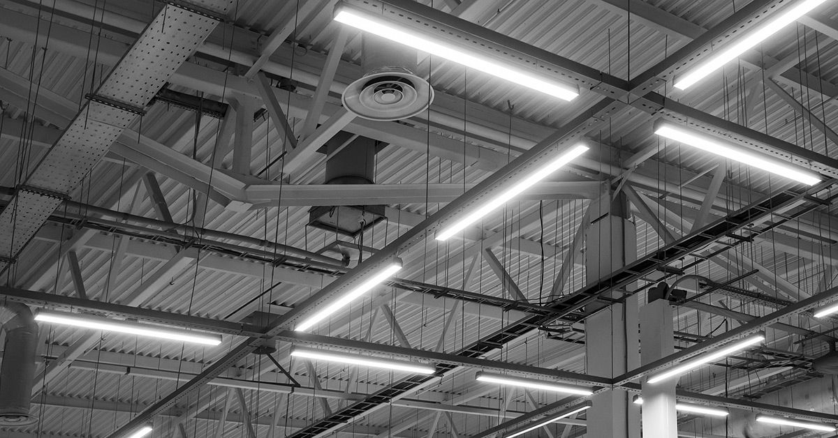 Industrial ceiling with fluorescent lighting designed to meet OSHA workplace lighting safety standards in a warehouse setting.