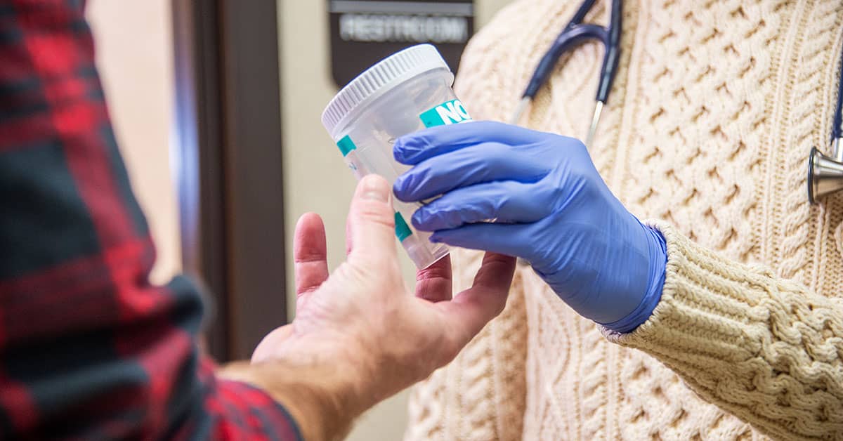 Healthcare worker handing urine sample container to patient for post-incident drug testing in clinical setting.