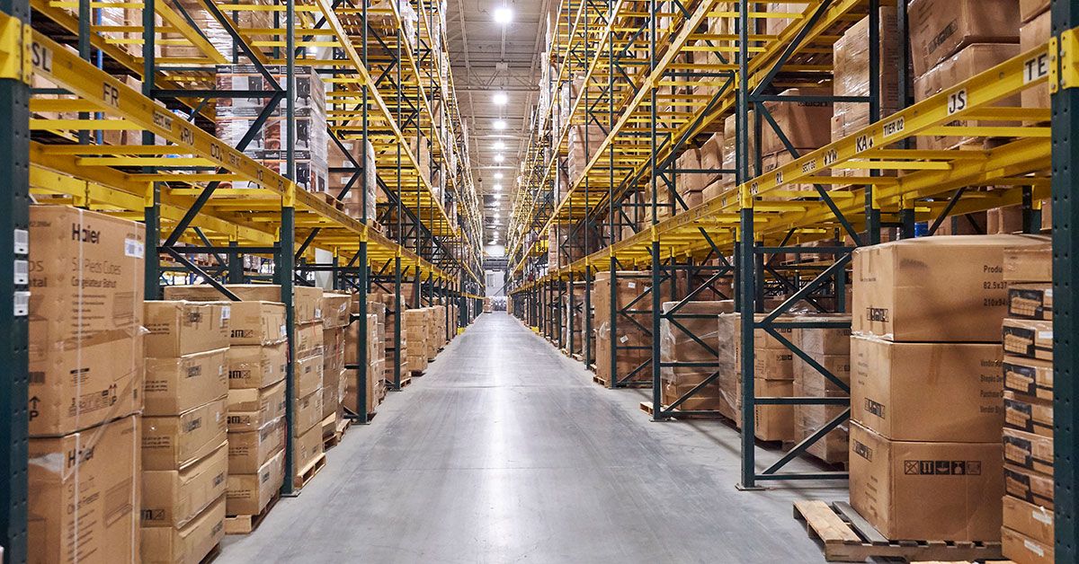 Interior view of a large warehouse with tall shelves filled with stacked cardboard boxes, showcasing organized storage and efficient use of space.