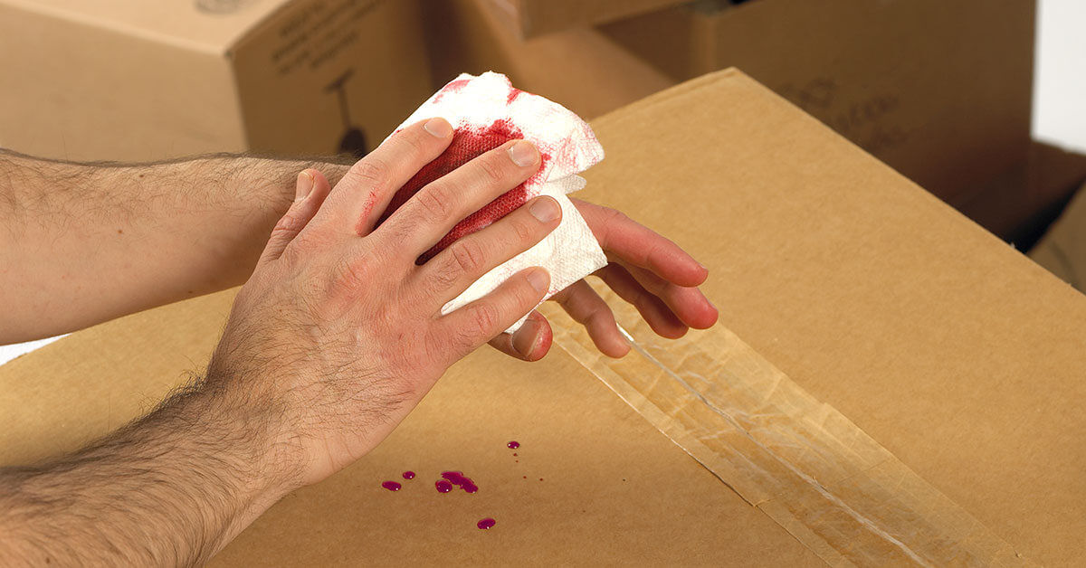 Worker treating a minor hand injury with tissue, highlighting potential bloodborne pathogen exposure in non-healthcare settings like moving or packing jobs.