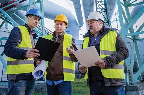 3 workers with hardhats and safety vests walking through production area with clipboards