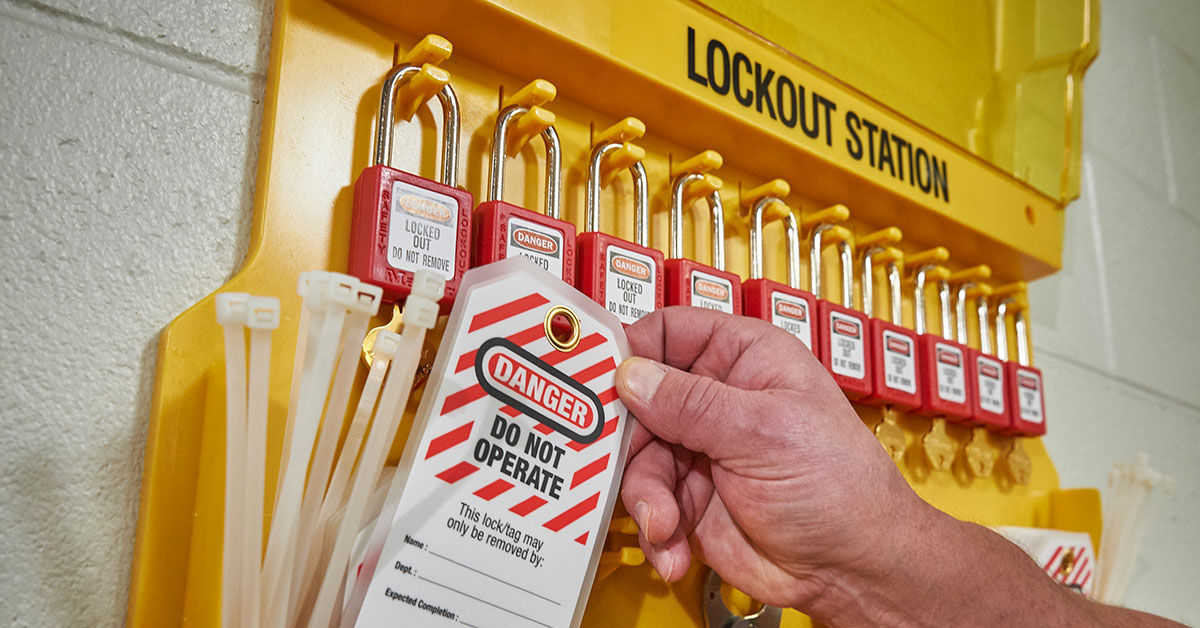 Lockout station with multiple red padlocks and a 'Danger Do Not Operate' tag being placed by a hand, ensuring workplace safety compliance.