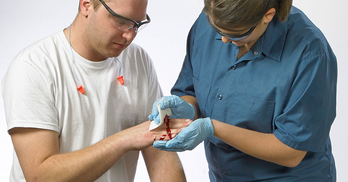 First aid treatment for a hand injury with bleeding, demonstrating proper wound care techniques using gloves and sterile gauze and the need for bloodborne pathogen training.