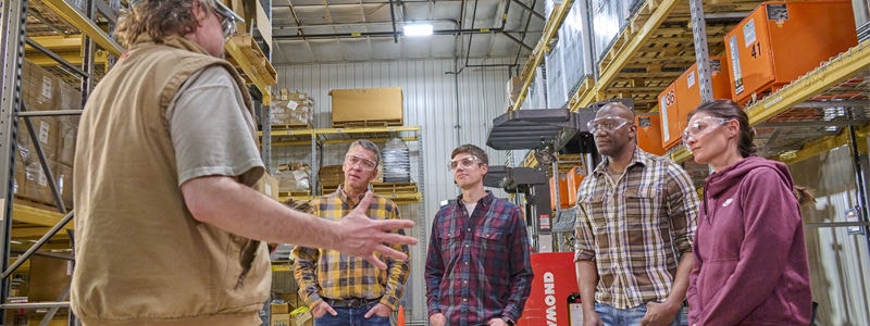 Warehouse safety toolbox talk in progress with supervisor briefing workers on safety protocols amid inventory shelves.