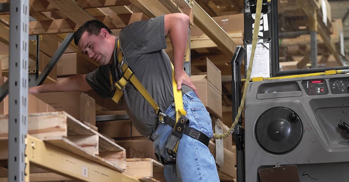 Warehouse worker showing signs of back pain while lifting a box, highlighting the need for light duty assignments after workplace injuries.