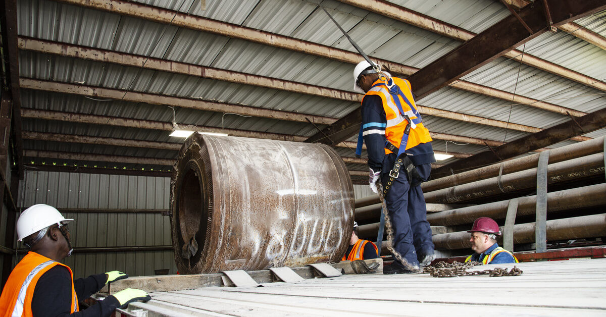 Workers in safety gear atop rolling stock in an industrial setting, illustrating fall protection considerations and OSHA compliance challenges.