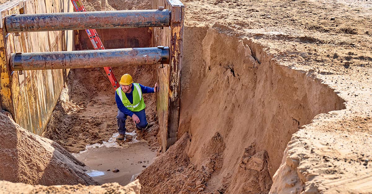 Construction worker in a trench with shoring equipment ensuring safety during excavation & trenching work.