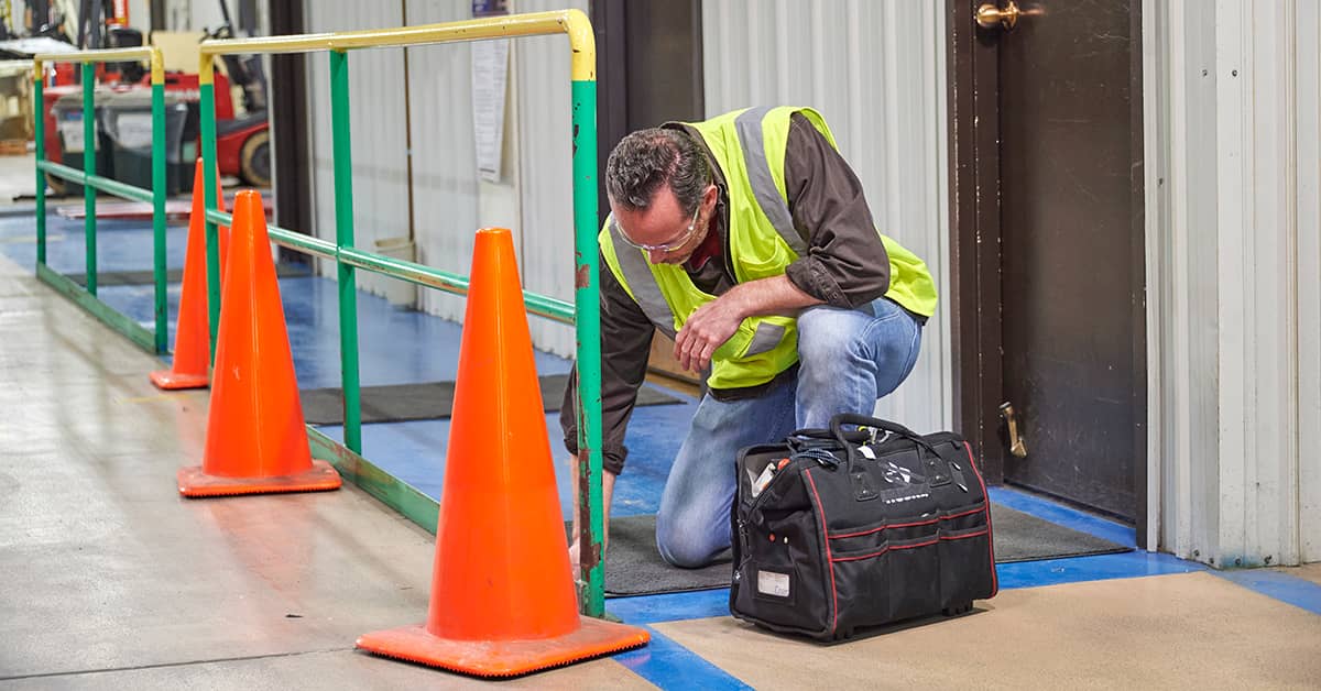 Worker inspecting guardrail during walking-working surface safety check in industrial facility.