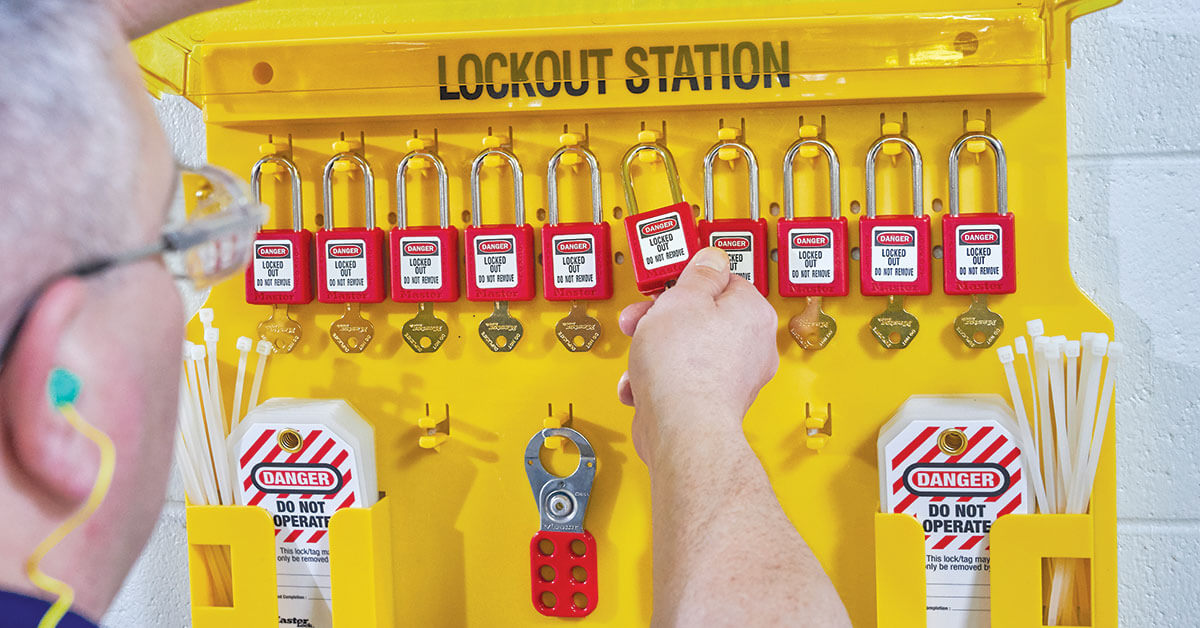Worker using a lockout/tagout station with padlocks and tagout tags for industrial safety compliance procedures.