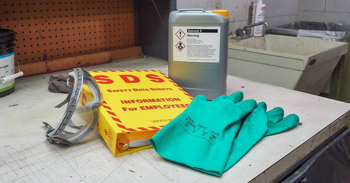 SDS Binder, Chemical container with hazcom label, and PPE on top of workspace