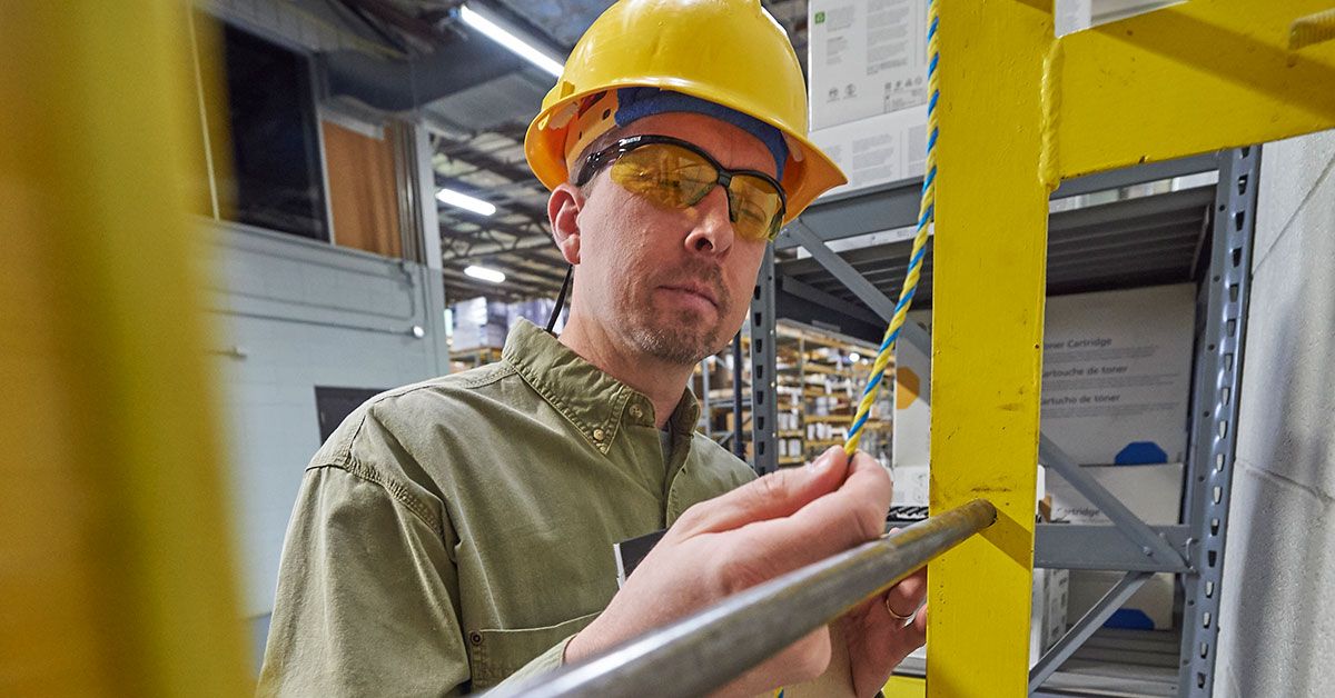 Warehouse worker inspecting safety rope on metal shelf—an example of a task suitable for job hazard analysis (JHA) in an industrial setting.