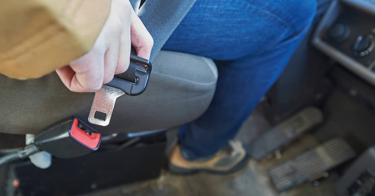 Person buckling seatbelt in a car, promoting workplace safety and compliance with a company vehicle safety program; close-up of hand and seatbelt latch.