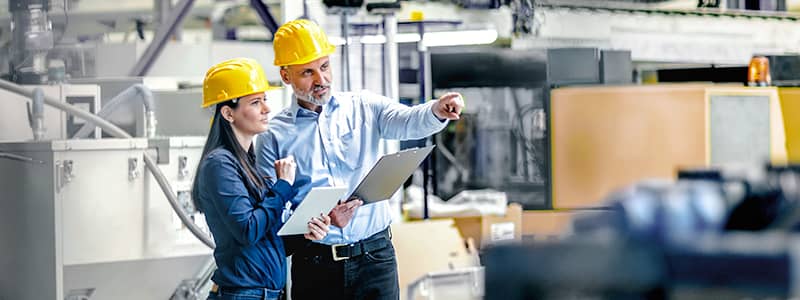 Two safety managers in hard hats reviewing workplace safety plans in an industrial facility, illustrating proactive safety management and compliance oversight.