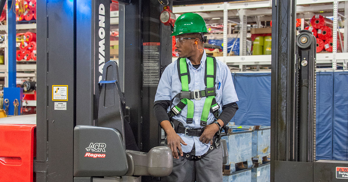 Warehouse worker in safety gear operating forklift, illustrating OSHA fall protection training in industrial settings.