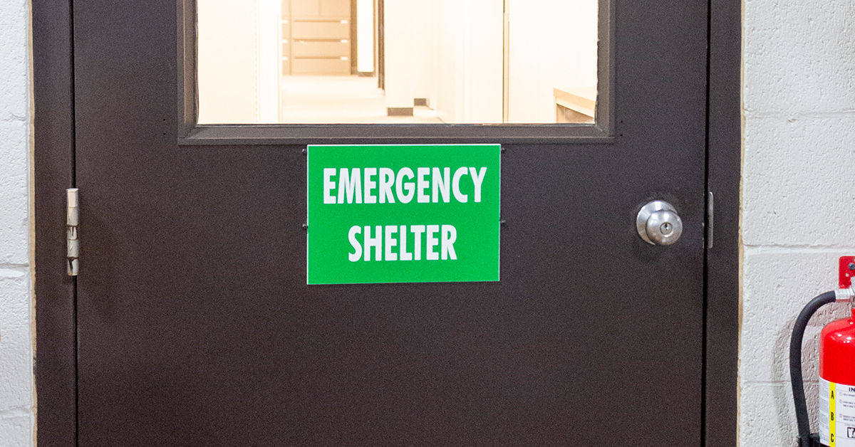 Emergency shelter door with green sign in a building hallway, featuring a fire extinguisher on the right side.