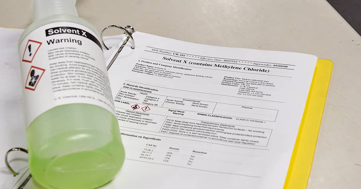 Solvent X bottle with hazard label resting on open binder displaying Chemical Safety Data Sheet (SDS)