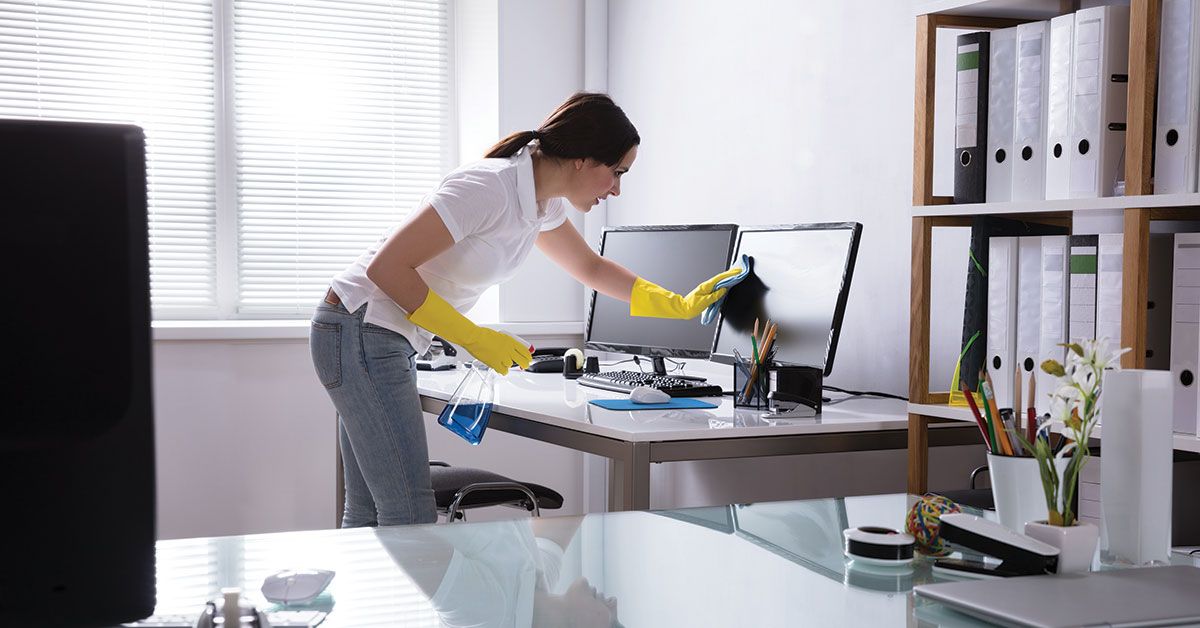 Employee cleaning an office workstation with household cleaning products