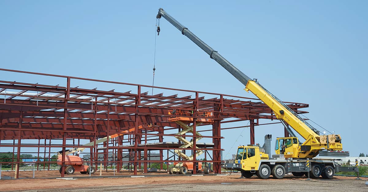 Construction crane lifting steel beams at job site, illustrating OSHA 1926 Subpart CC crane safety compliance