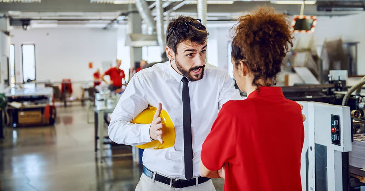 Supervisor holding hard hat speaking accusatory to a worker