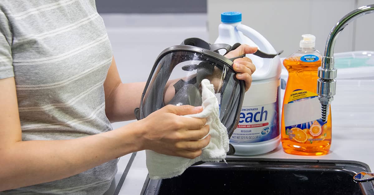 Woman cleaning respiratory protection in a sink with bleach and dish soap