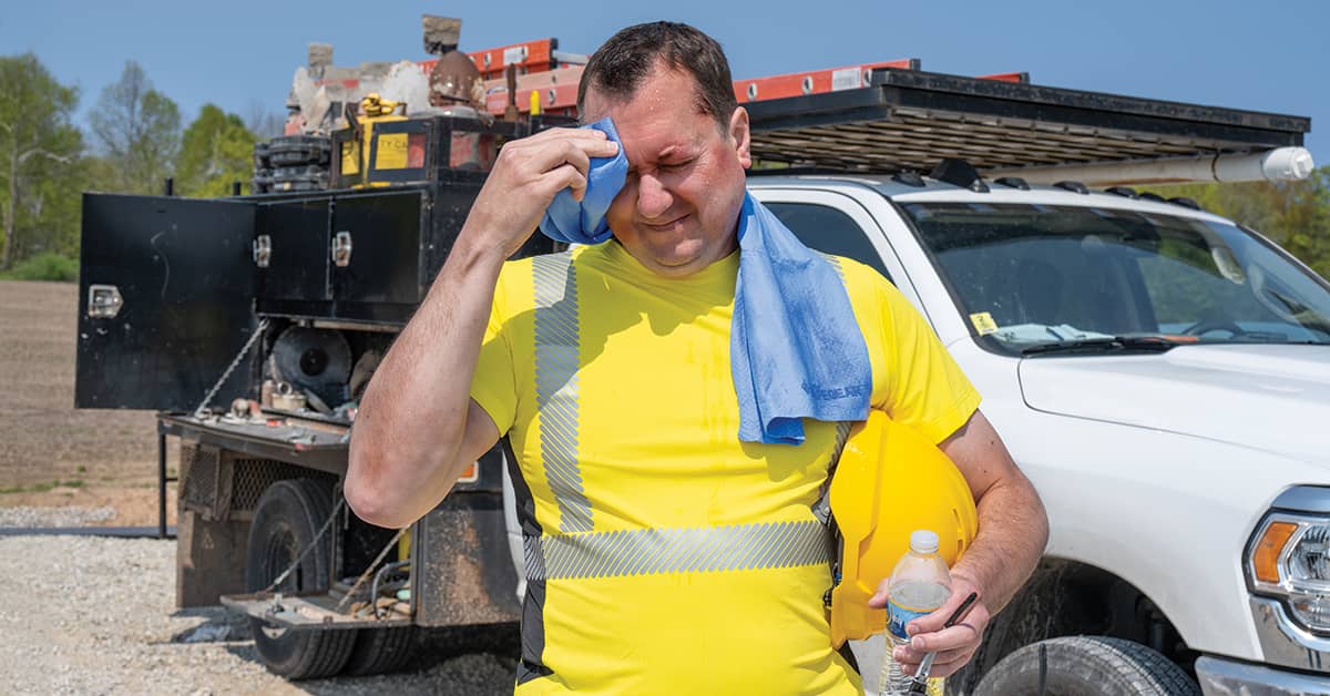 Outdoor worker in high-heat conditions, wearing safety vest and holding water bottle—illustrating OSHA heat illness prevention in outdoor workplaces.