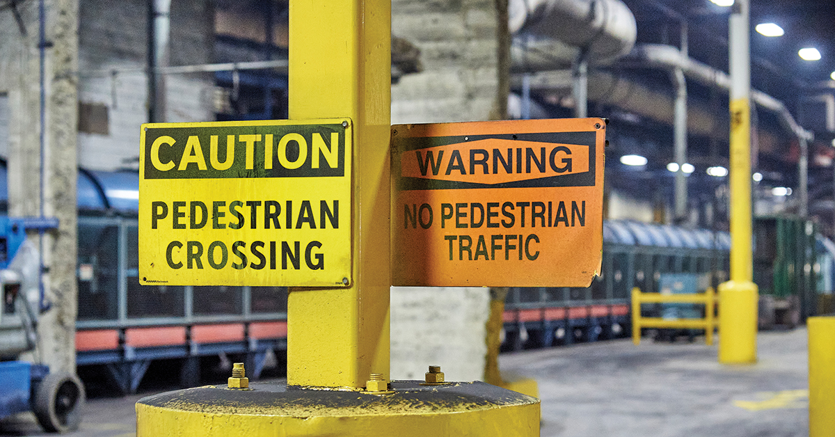 Industrial workplace with OSHA-compliant caution and warning signs on a yellow pole, highlighting pedestrian safety and hazard awareness.
