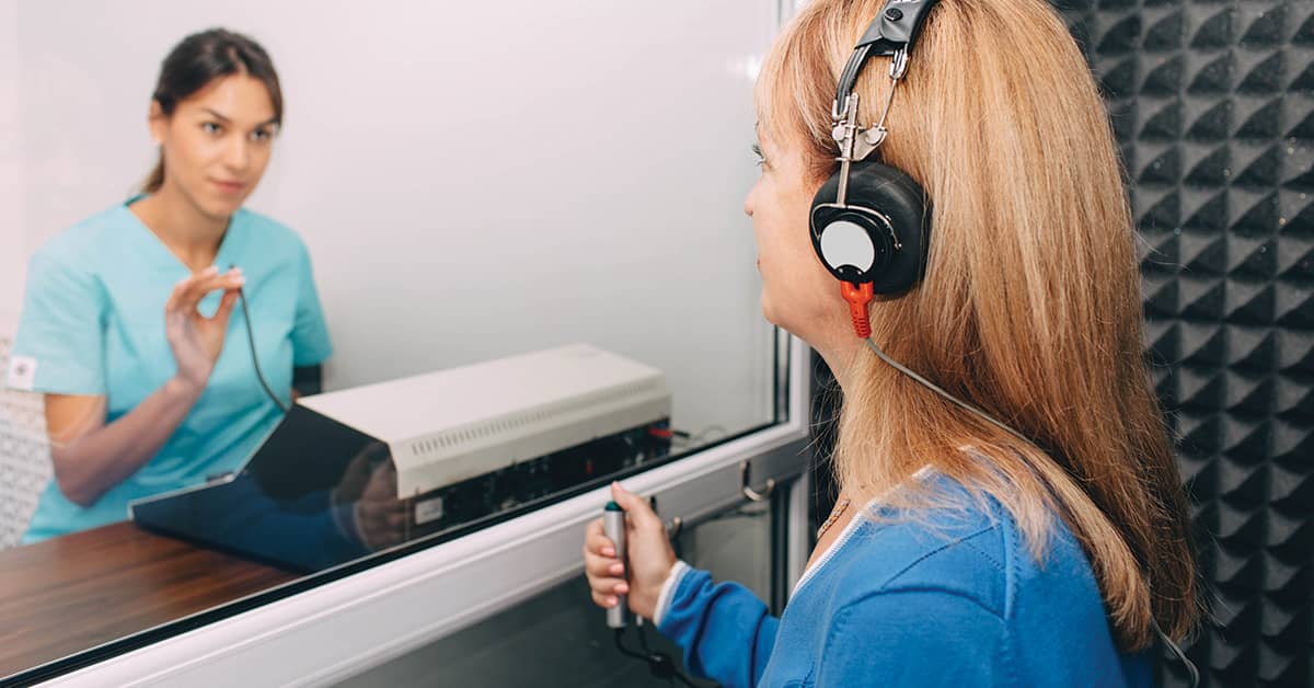 Audiologist doing hearing exam to a patient using audiometer in special audio room